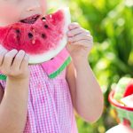Young girl in pink summer dress eats watermelon. Yum!